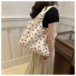 Detailed close-up of off-white corduroy tote bag with red strawberry pattern textures