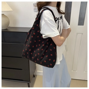 Detail of black corduroy tote bag with red strawberry print shown on model's shoulder