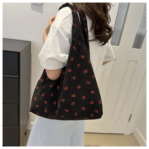 Close-up of black corduroy tote bag with red strawberry pattern and spacious design