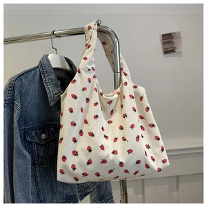 Detail of white corduroy tote bag featuring red strawberry print and soft ribbed texture