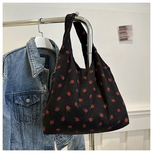 Detail of strawberry print on black corduroy tote bag hanging against white wall