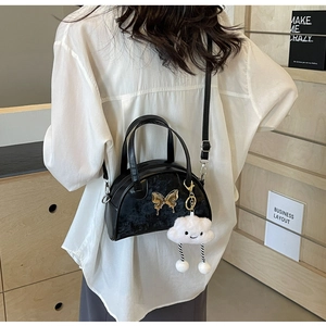 Close-up of black leather crossbody bag with golden butterfly and plush cloud charm