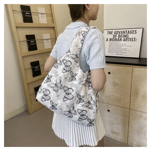 Detail view of white lace tote bag with black butterfly embroidery on woman's shoulder