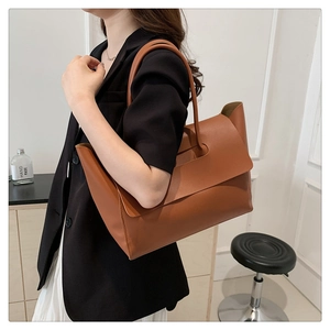 Detailed view of brown leather tote bag with flap design worn by model for commuting