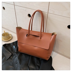 Detail of a brown leather tote bag with a folding flap design on a black leather jacket