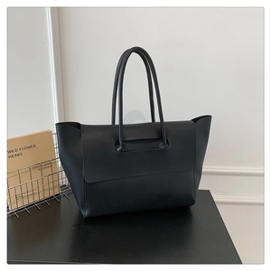 Detail of matte black leather tote bag with unique handle-connected flap on a wooden table