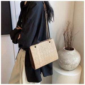 Detail of woven straw tote bag featuring V-shaped texture and gold chain shoulder straps