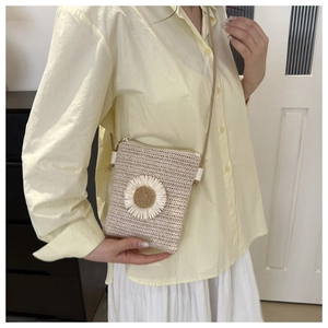 Model wearing a beige straw crossbody bag featuring delicate sunflower floral applique