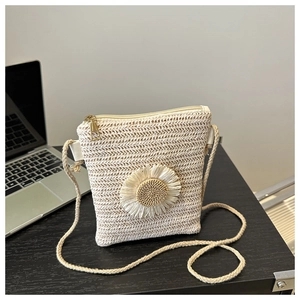 Detail of hand-woven beige straw crossbody bag featuring a 3D white daisy floral ornament