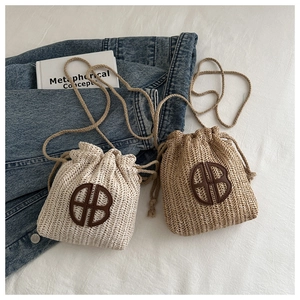 Détail de mini sacs en paille tissée avec patch logo en cuir et fermeture par cordon