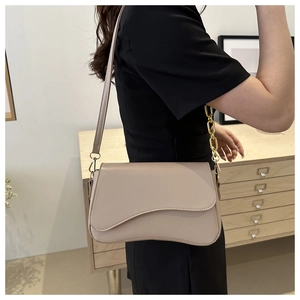 Detail showing asymmetric wave flap and gold chain strap on beige crossbody bag