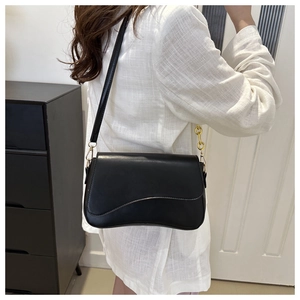 Detail of black wave-pattern flap bag with gold metal buckle on female model