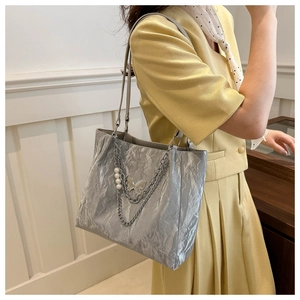 Dettaglio della borsa tote argento plissettata con ciondolo a farfalla e perle metalliche