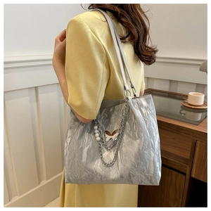 Dettaglio della borsa tote argento con texture metallica, catena di perle e farfalla