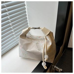 Detail of floral jacquard handbag with metallic buckle and decorative beaded tassel charm