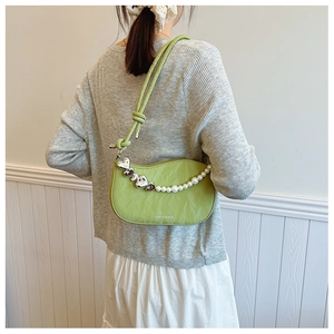Model wearing a green half-moon shoulder bag with heart charms and pearl chain