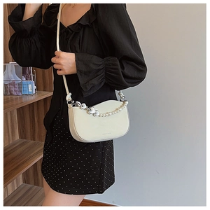 Detail of beige crescent bag featuring faux pearl chain and heart metal charm on model