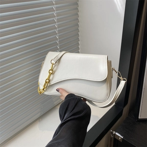 Minimalist white leather crossbody bag with bold gold chain detail shown in hand