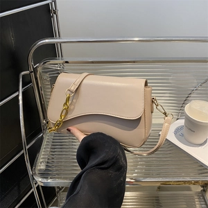 Chic beige crossbody bag with gold chain strap and soft flap design on a modern display
