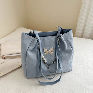 Borsa tote celeste con fibbia a farfalla e catena di perle appoggiata sul letto