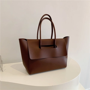 Detail of dark brown tote bag showing matte texture, long handles, and large top flap