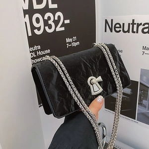 Minimalist black quilted chain crossbody bag with metallic clasp held against poster wall