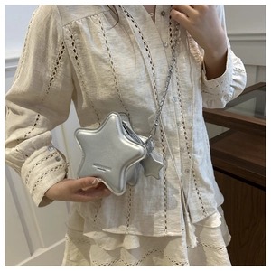Detail of silver star-shaped crossbody bag with metal chain strap worn by a model