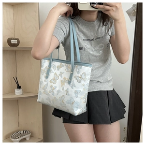 Detail of blue butterfly embroidery on white canvas tote bag with blue leather handle