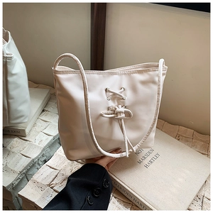 Detail of off-white ballet style bucket bag featuring lace-up knot and pearly texture