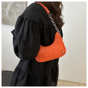 Model wearing bright orange crescent bag with silver chain and sleek leather finish
