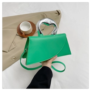 Close-up of green leather handbag with a unique silver sculptural metal handle in use