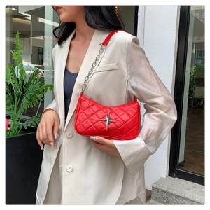 Outdoor shot of a red quilted shoulder bag featuring a silver star buckle and chain strap