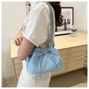 Detail shot of a light blue bucket bag with a large bow worn by a model in a cozy setting