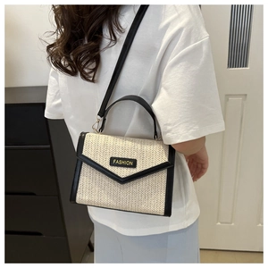 Détail d'un sac bandoulière tissé bicolore avec bordure en cuir noir et poignée chic
