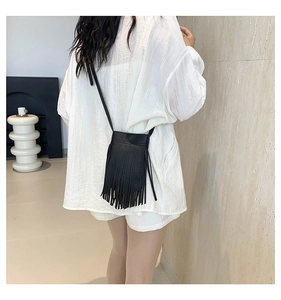 Detail van zwarte crossbody tas met lange franjes en kiezellederen textuur gedragen door model