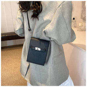 Détail d'un mini sac bandoulière noir avec fermoir argenté porté sur un blazer gris chic