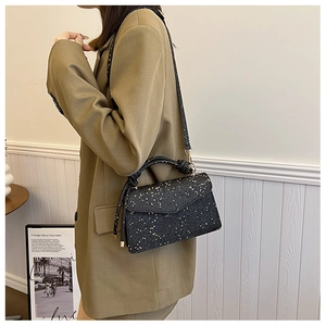 Detail of black sequined handbag with gold hardware styled on olive green blazer