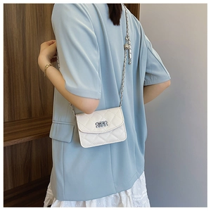 Détail d'un sac bandoulière matelassé avec chaîne argentée porté avec un blazer bleu clair