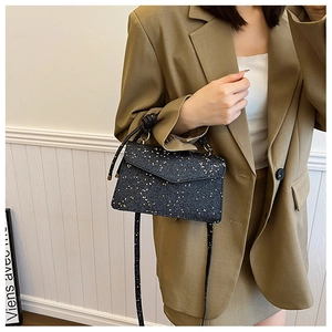 Detail of elegant black sequin handbag with gold shimmer and metallic handle on a brown blazer