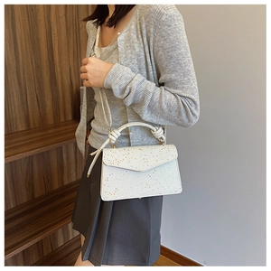 Detail of white glitter handbag with woven handle and envelope flap on wooden display