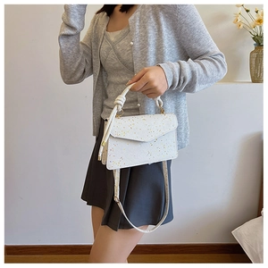 Detail of white glossy handbag featuring knot handle design and shimmering glitter accents