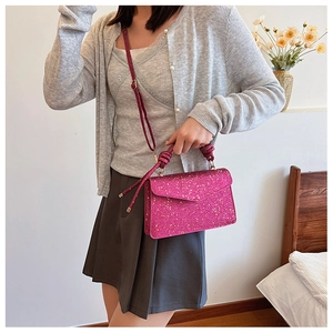 Close-up of a vibrant magenta sequined handbag with knotted handle and shoulder strap