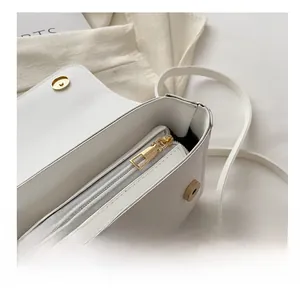 Detail view of smooth golden zipper and magnetic closure on white faux leather square bag