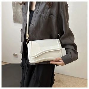 Close-up of white minimalist flap bag with curved trim and gold metal buckle on model