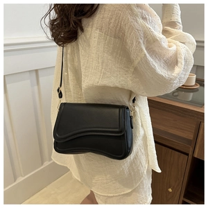 Detail of minimalist black crossbody bag with asymmetric wavy flap and thin shoulder strap