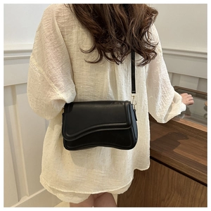 Detail of minimalist black crossbody bag with wavy flap edge and gold hardware