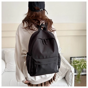 Detail of black nylon backpack featuring white fashion label on a side pocket
