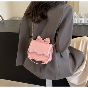 Pink crossbody bag with wavy flap and 3D bow detail shown from a rear model view