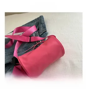 Dettaglio della borsa a cilindro rosa con tracolla larga in tessuto su denim