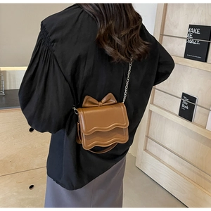 Macro detail of brown mini crossbody bag with wave flap, bow, and gold chain strap